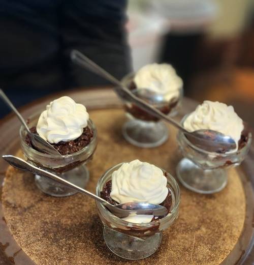Four small glass bowls of chocolate dessert topped with whipped cream, placed on a round tray.