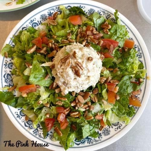 A colorful salad with greens, tomatoes, and a mound of creamy chicken salad topped with pecans on a decorative plate.