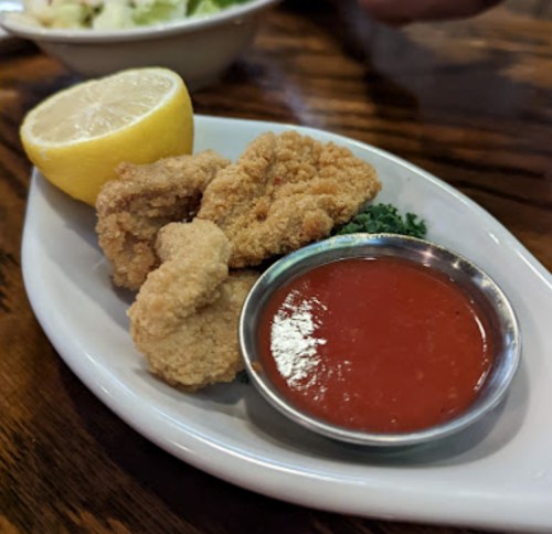 Fried seafood pieces on a plate with a lemon wedge and a small bowl of red dipping sauce.