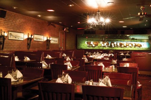 Cozy restaurant interior with red booths, tables set with white napkins, and a mural of cows on the wall.