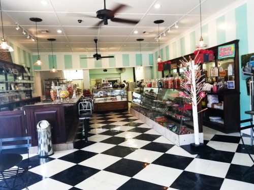 A colorful candy shop interior with a checkered floor, display cases, and shelves filled with sweets and treats.