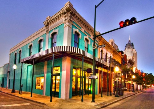 Colorful building at dusk with a striped awning, streetlights, and a city skyline in the background.