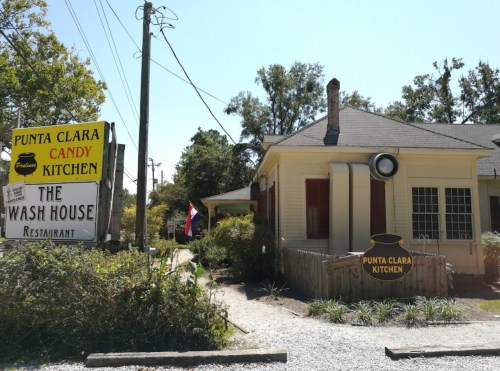 A quaint restaurant with a sign reading "Punta Clara Kitchen" and "The Wash House," surrounded by greenery.