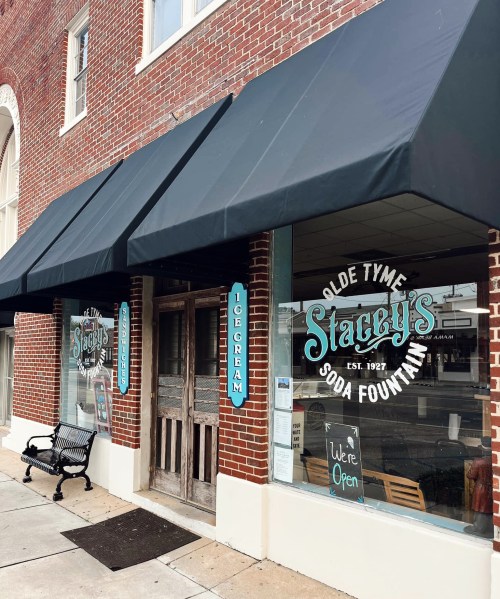 Exterior of Stacey's Olde Tyme Soda Fountain, featuring a brick facade, awnings, and a sign indicating it's open.