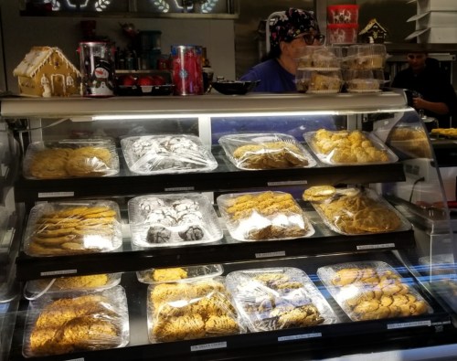 A display case filled with various cookies, neatly arranged and covered, with a person in the background.