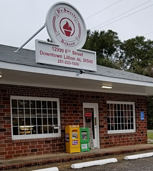 A brick bakery storefront with a sign displaying the name, address, and contact information.