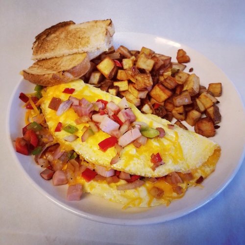 A plate of a cheese and ham omelette, diced potatoes, and toasted bread.