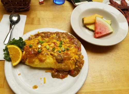 A large omelette topped with cheese and salsa, served with a side of fruit including watermelon and cantaloupe.