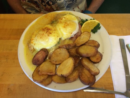A plate of eggs Benedict with hollandaise sauce, served with roasted potatoes and a lemon wedge.