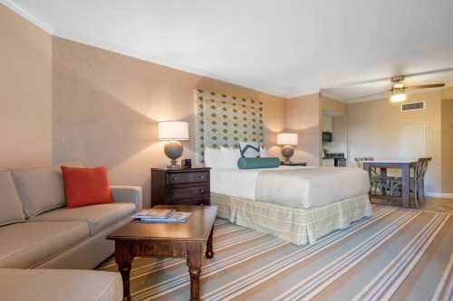 A cozy hotel room featuring a king bed, sofa, wooden table, and warm decor with soft lighting.