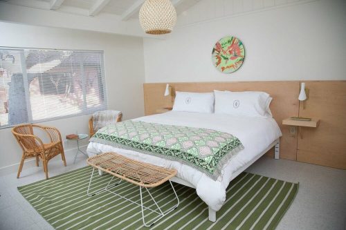Bright, modern bedroom with a large bed, green patterned throw, wicker chairs, and a round wall art piece.