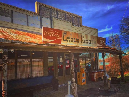 A rustic storefront of Lotham Mercantile with a Coca-Cola sign, featuring a wooden porch and blue sky in the background.