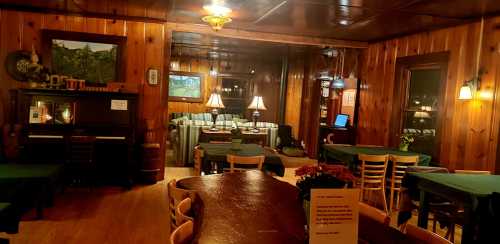 Cozy wooden dining room with tables, a piano, lamps, and a floral centerpiece, creating a warm, inviting atmosphere.