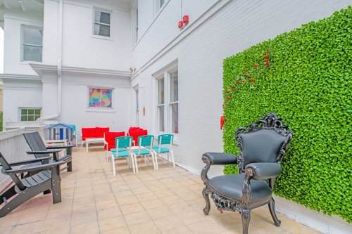 A stylish outdoor patio with a black chair, colorful seating, and a green wall feature.