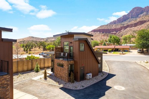 Modern two-story building with a unique design, surrounded by mountains and greenery under a clear blue sky.