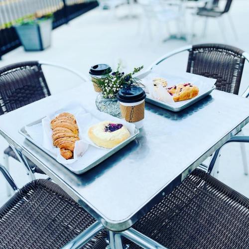 A table with two trays of pastries and coffee cups, surrounded by outdoor seating.