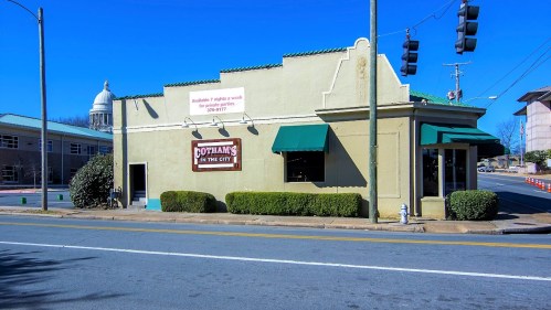 A small, light-colored building with green awnings and a sign reading "Gotham's in the City" on a sunny street.