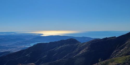 A panoramic view of mountains and a shimmering ocean under a clear blue sky.
