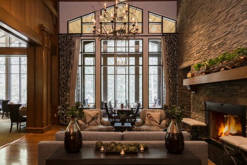 Cozy interior with a stone fireplace, large windows, and elegant decor, featuring a chandelier and comfortable seating.
