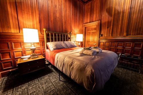 Cozy bedroom with wooden walls, a double bed, bedside lamps, and neatly folded towels on the bed.