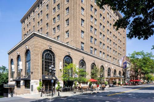 Historic brick building with large arched windows, outdoor seating, and trees lining the street on a sunny day.
