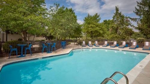 A clear swimming pool surrounded by lounge chairs and tables, set in a green, landscaped area under a cloudy sky.