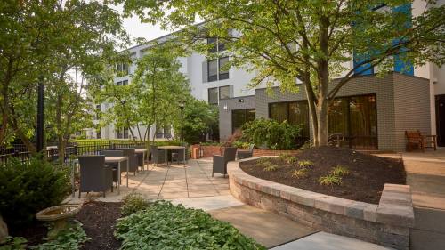 A landscaped outdoor area with seating, trees, and a pathway beside a modern building.