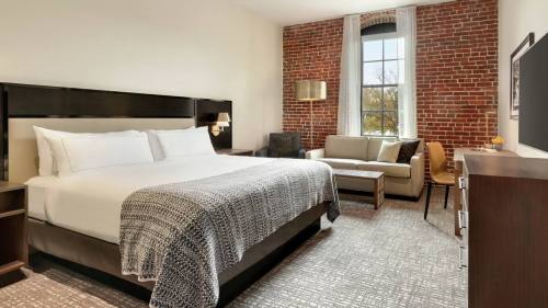 Cozy hotel room featuring a king bed, seating area, and exposed brick walls with natural light from a large window.