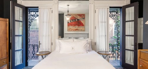 Cozy bedroom with a white bed, large windows, and decorative artwork, featuring elegant doors and natural light.