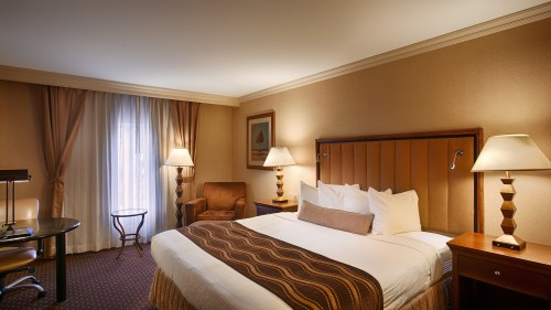 Cozy hotel room featuring a bed, armchair, desk, and lamps, with soft lighting and curtains.