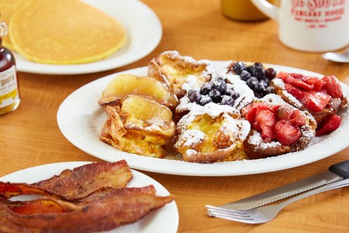 A plate of French toast topped with berries and powdered sugar, alongside crispy bacon and a stack of pancakes.