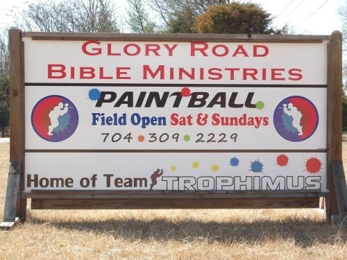 Sign for Glory Road Bible Ministries featuring paintball field hours, contact info, and Team Trophimus.