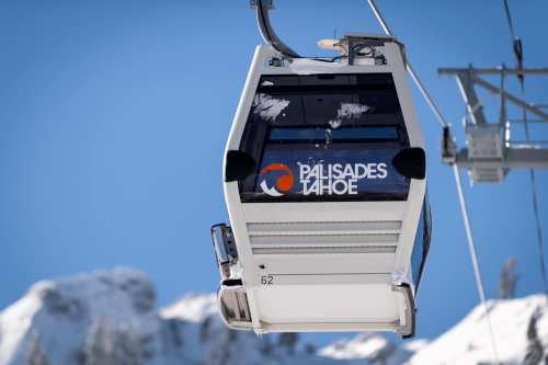 A gondola lift at Palisades Tahoe against a clear blue sky and snowy mountain backdrop.