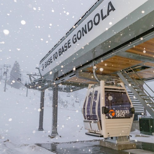 A gondola station in a snowy landscape, labeled "Base to Base Gondola," with snowflakes falling around it.