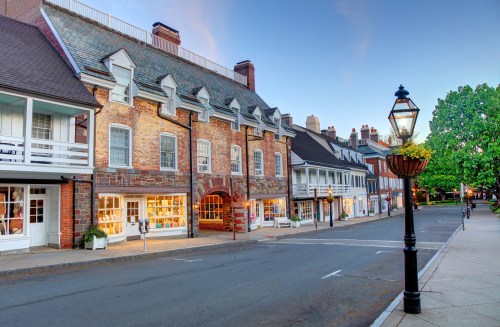 Historic buildings line a quiet street, with charming architecture and a lamppost adorned with flowers.