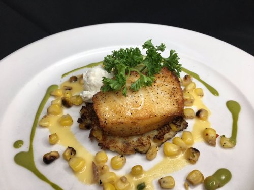 A beautifully plated dish featuring seared fish on a bed of corn, garnished with herbs and a drizzle of sauce.