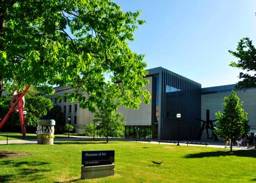 A sunny view of the Museum of Art, featuring modern architecture and sculptures in a green park setting.