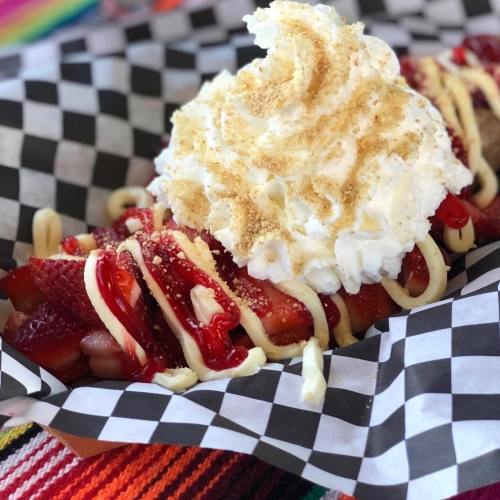A dessert featuring strawberries topped with whipped cream, drizzled with sauce, and sprinkled with crumbs in a checkered paper.