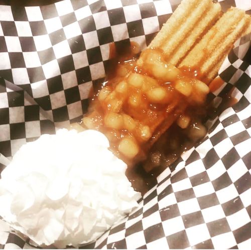 Churros topped with apple pie filling and whipped cream, served in a checkered paper basket.