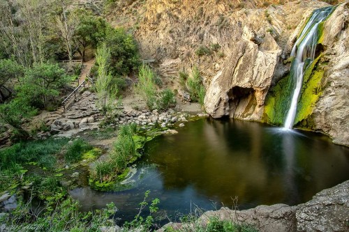A serene waterfall cascades into a tranquil pool, surrounded by lush greenery and rocky cliffs.