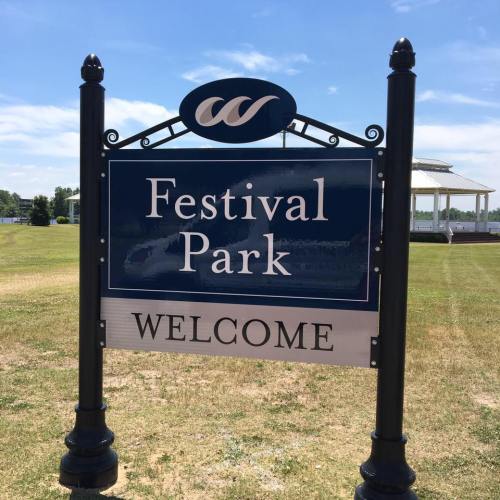 Sign for Festival Park with "Welcome" displayed, set against a clear blue sky and grassy field.