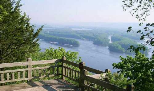 Scenic view from a wooden overlook, featuring a river winding through lush green trees and hills in the distance.