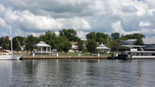 A serene waterfront scene featuring gazebos, trees, and boats under a partly cloudy sky.