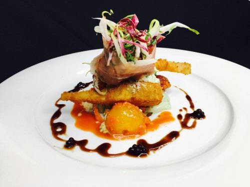 A gourmet dish featuring crispy fried elements, colorful garnishes, and a drizzle of sauce on a white plate.