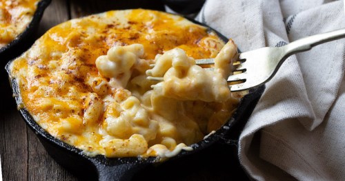 Creamy macaroni and cheese in a cast iron skillet, with a fork lifting a cheesy pasta bite.