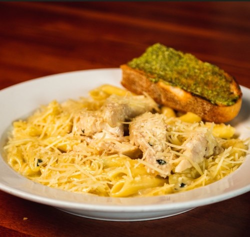 A plate of creamy pasta with chicken and grated cheese, accompanied by a slice of garlic bread topped with pesto.