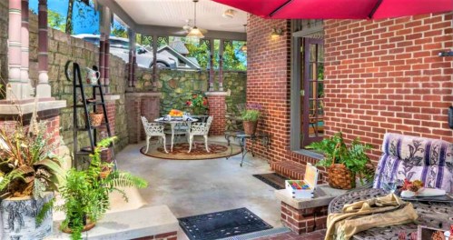 Cozy outdoor patio with a dining table, chairs, potted plants, and a red umbrella, surrounded by brick walls.