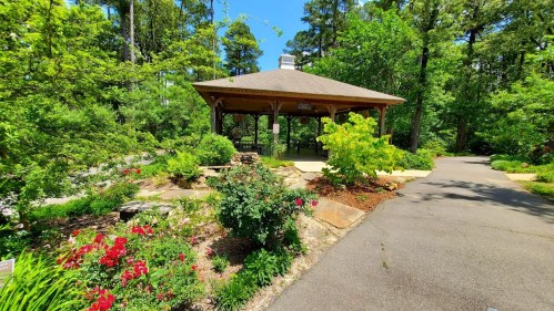 A gazebo surrounded by lush greenery and colorful flowers along a paved path in a serene garden setting.