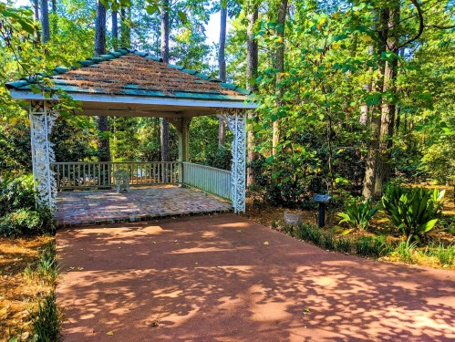 A serene gazebo surrounded by lush greenery and trees, with a stone pathway leading up to it.