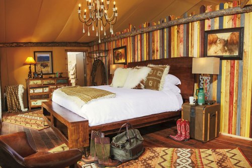Cozy tent bedroom with a wooden bed, colorful striped walls, rustic decor, and warm lighting.